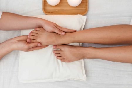 Young woman having feet and legs massage in beauty spa salon, close up. Masseur kneads the foot and leg of a young beautiful girl at candle background, top view