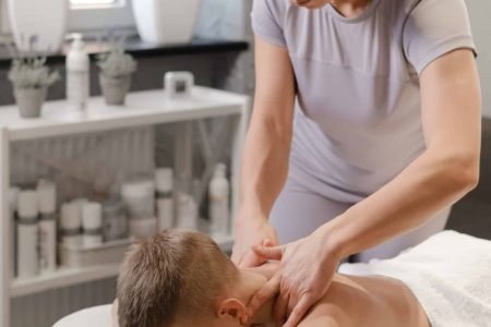 masseur gives the child a back massage. Kids massage concept. massage therapist giving 7 year old boy shoulder massage. Physical therapy